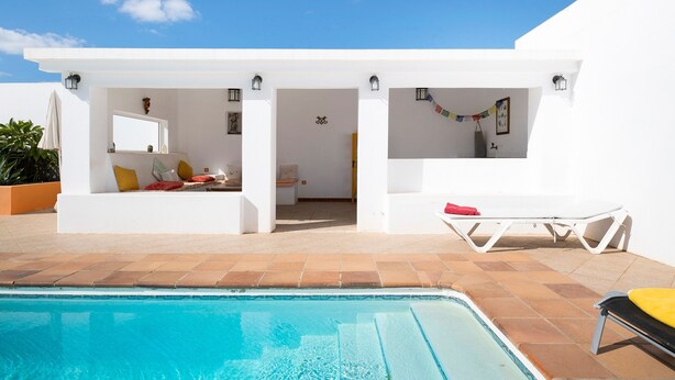Zona junto a la piscina con una piscina azul cristalina, paredes blancas y techo blanco.
