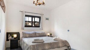 Un dormitorio con cama, mesitas de noche, una ventana con cortinas, una araña y un pequeño adorno en la pared.