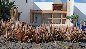 A modern building with a white facade, a chimney, and a small patio area with cacti and succulents. - Casa Sol Y Mar: Sea Views, Private Pool & Wi-Fi in Lanzarote (Tías)