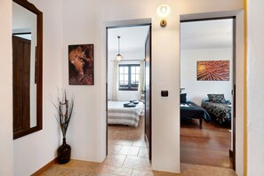 A hallway leading to a bedroom with a bed, a nightstand, and a wall-mounted light fixture.