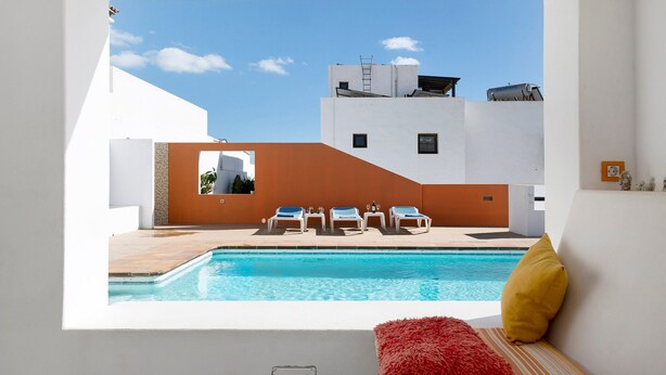A modern pool area with a clear view of the sky, a white building, and a red cushion. - Casa Sol Y Mar: Sea Views, Private Pool & Wi-Fi in Lanzarote (Tías)