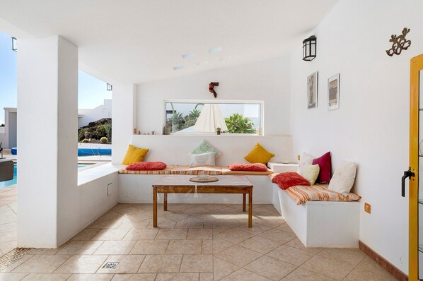 A room with a large window, a wooden table, and a sofa with cushions.