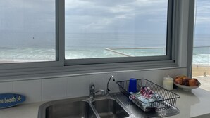 Ett kök med ett stort fönster med utsikt över havet, en diskho och en fruktskål på bänkskivan.