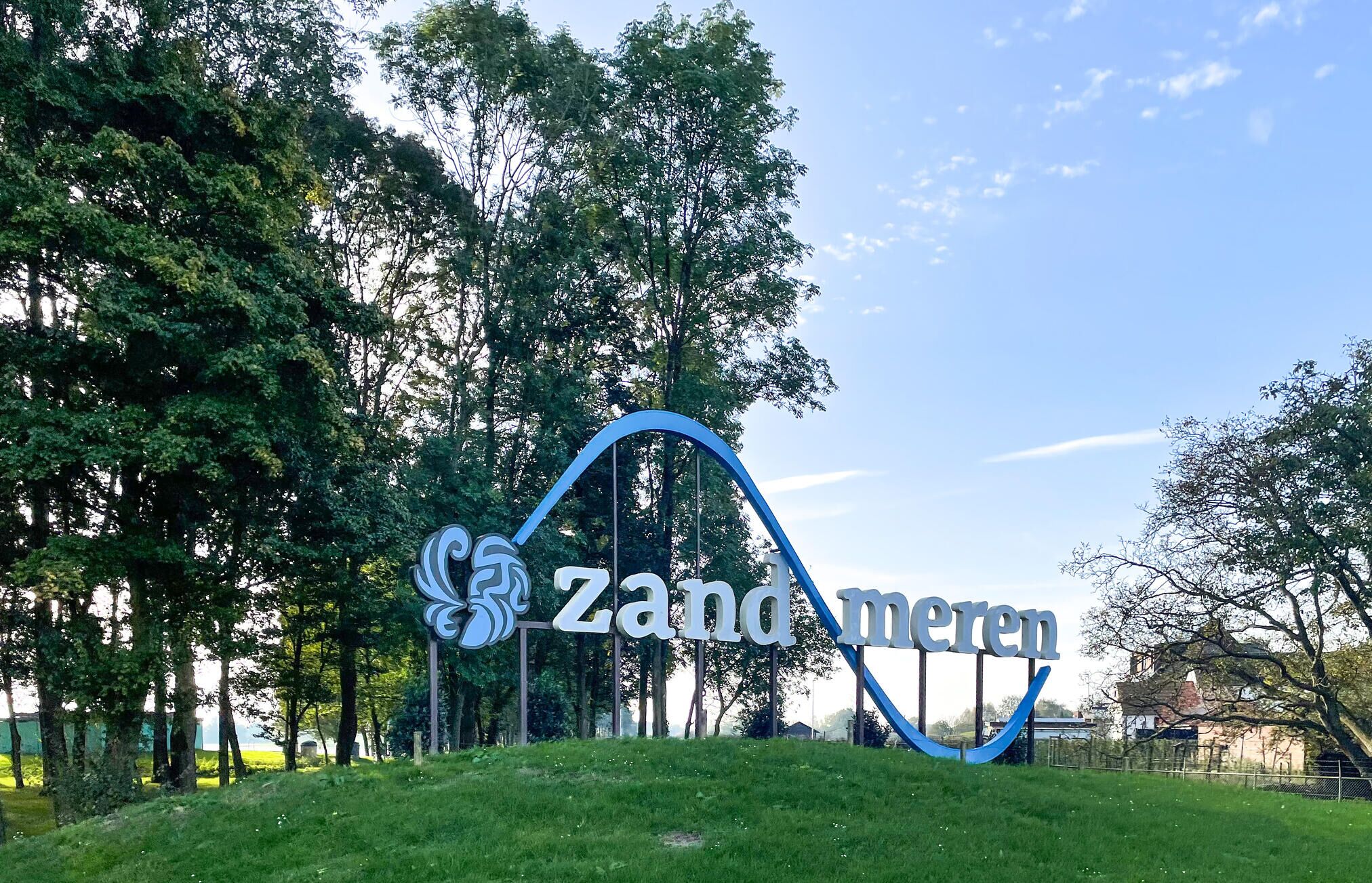 A large, curved sign with the text "Zandmeren" in the center, surrounded by greenery and trees.