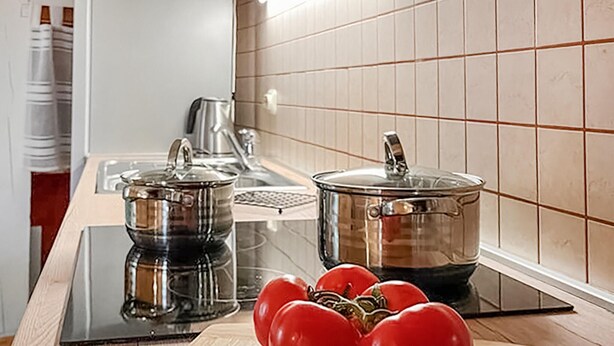 Una cocina con dos ollas de acero inoxidable sobre una cocina por inducción, un hervidor y una tabla de cortar con tomates.