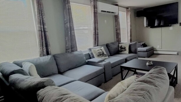 A modern living room with a grey sectional sofa, a small coffee table, and a flat-screen TV mounted on the wall. - Grand Trunk Cottage - a home for all seasons! (Gorham)