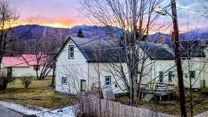 A rural house with a red roof, surrounded by bare trees and a mountain range in the background. - Grand Trunk Cottage - a home for all seasons! (Gorham)