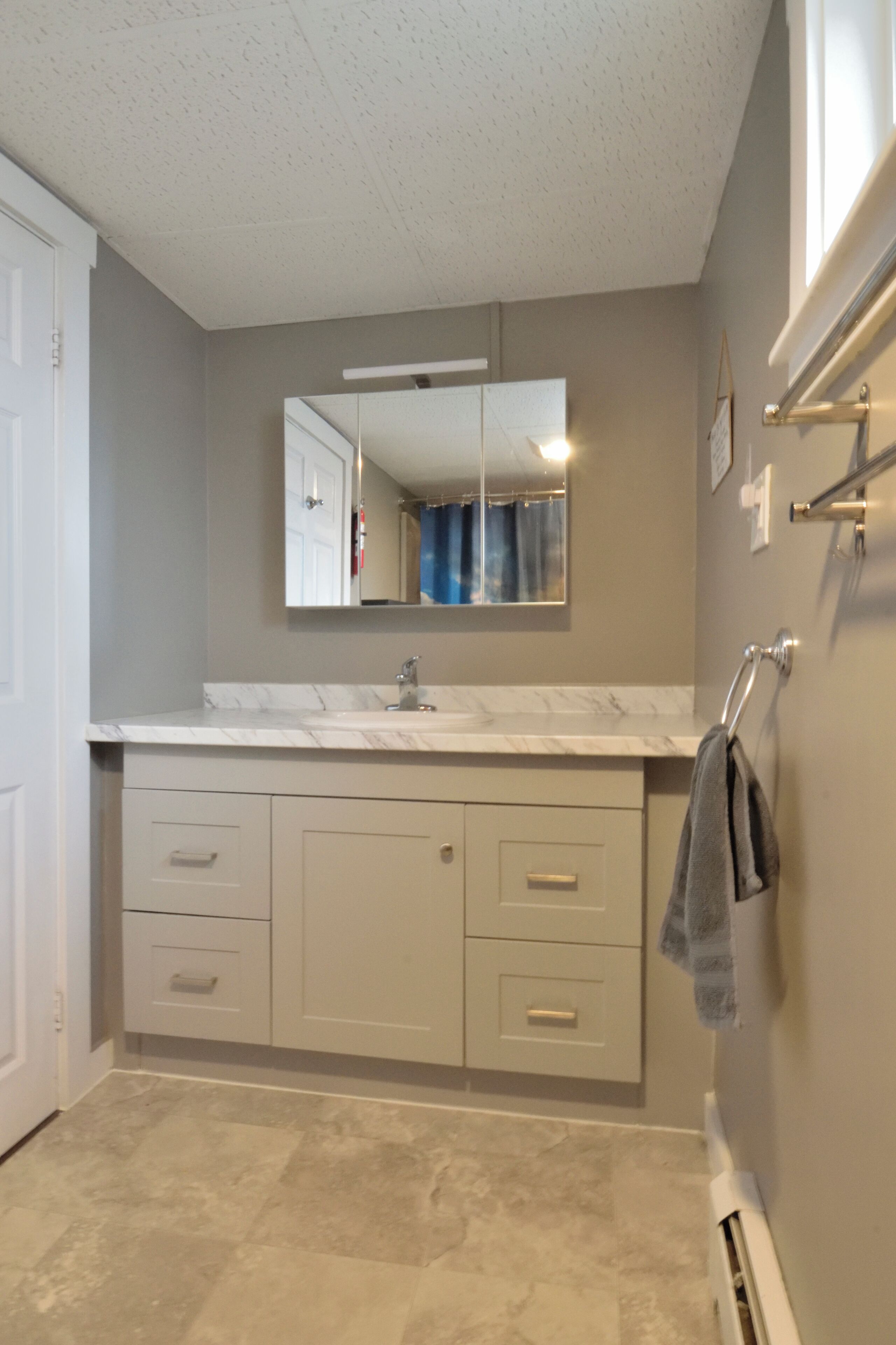 A bathroom with a marble countertop, a sink, a mirror, and a towel rack.