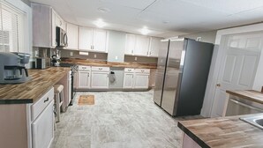 A modern kitchen with white cabinets, a stainless steel refrigerator, and a wooden countertop. - Grand Trunk Cottage - a home for all seasons! (Gorham)