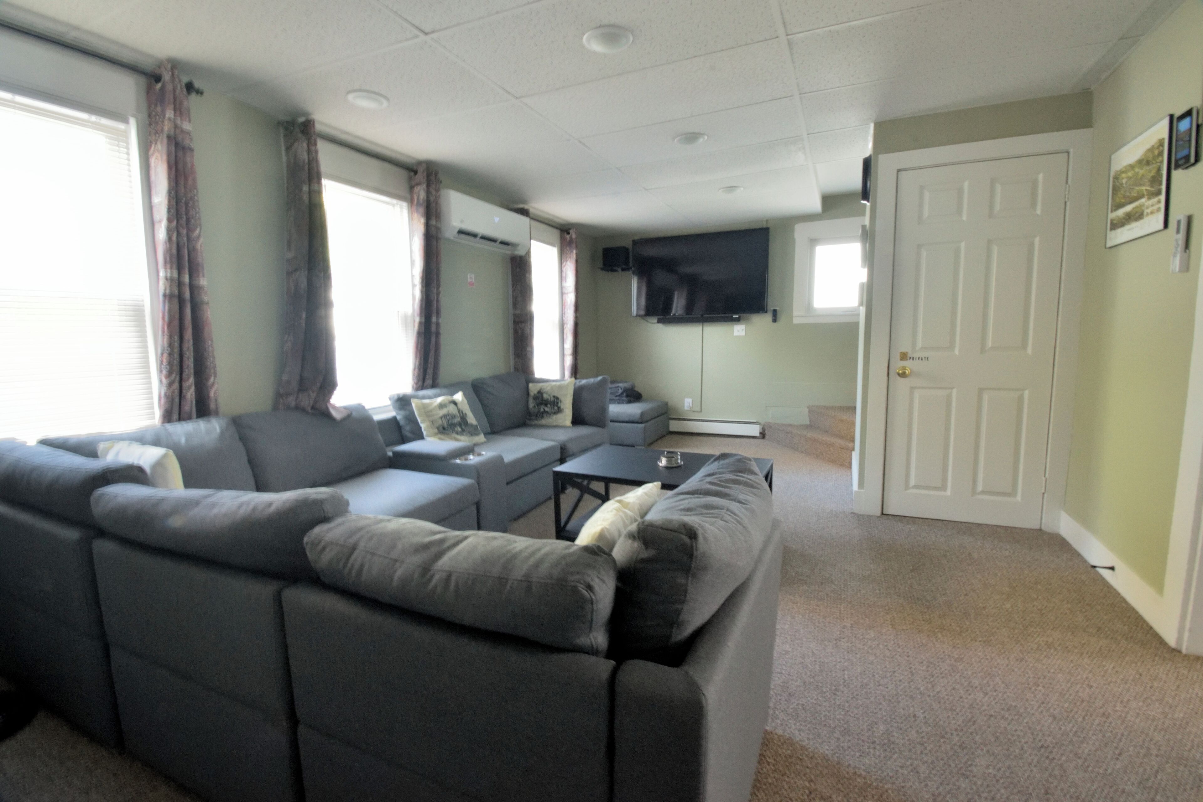 A living room with a sectional sofa, a flat-screen TV, and a door to the right.