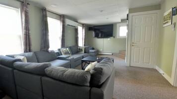 A living room with a sectional sofa, a flat-screen TV, and a door to the right.