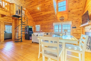 Ein gemütliches Blockhaus mit Wendeltreppe, Essbereich und Wohnzimmer mit Sofa und Fernseher.