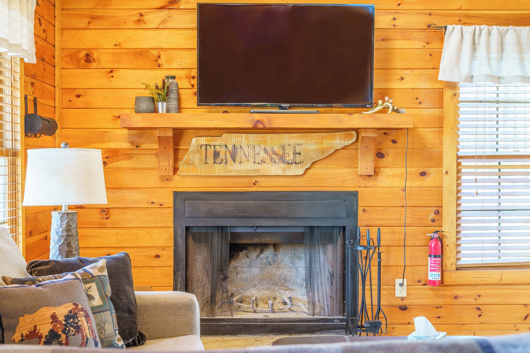L’intérieur chaleureux d’un chalet avec une cheminée, un téléviseur fixé au mur et une enseigne sur laquelle on peut lire « Tennessee ».