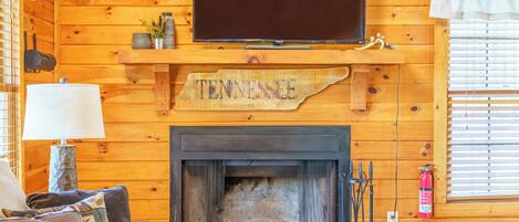 L’intérieur chaleureux d’un chalet avec une cheminée, un téléviseur fixé au mur et une enseigne sur laquelle on peut lire « Tennessee ».