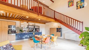 Una cocina amplia con electrodomésticos modernos, un comedor con sillas de colores y una escalera de madera.