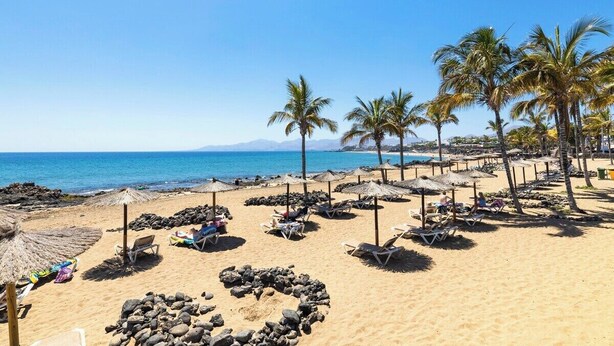 A beach with sun loungers and umbrellas, a clear sky, and a calm sea.