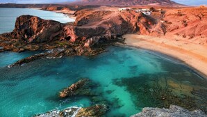 A coastal landscape with a beach, rocky shoreline, and a mountain in the background.