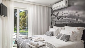 A modern hotel room with a large bed, a flat-screen TV, and a view of greenery through the window.