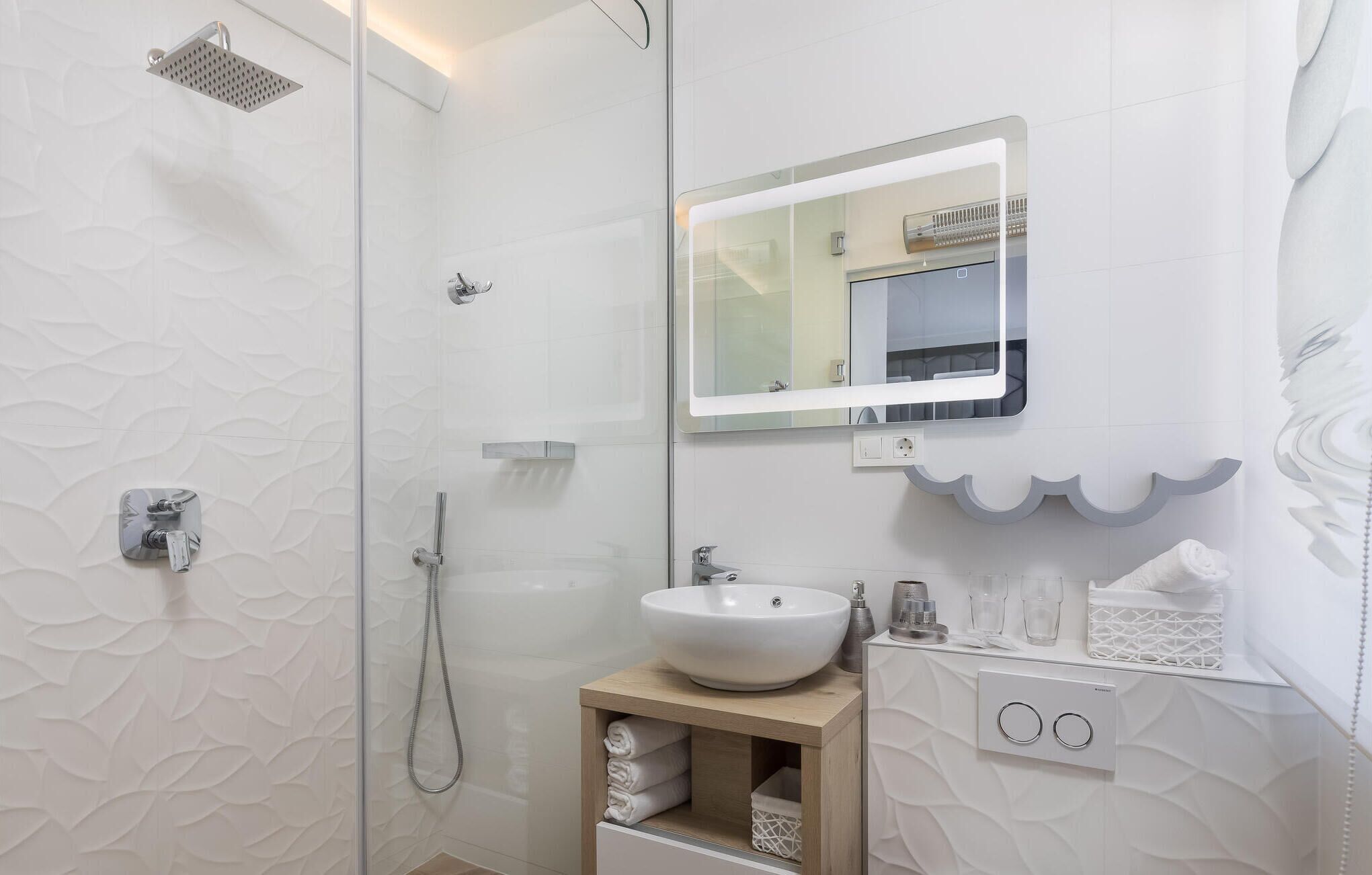 A modern bathroom with a glass-enclosed shower, a white sink, and a mirror above it.
