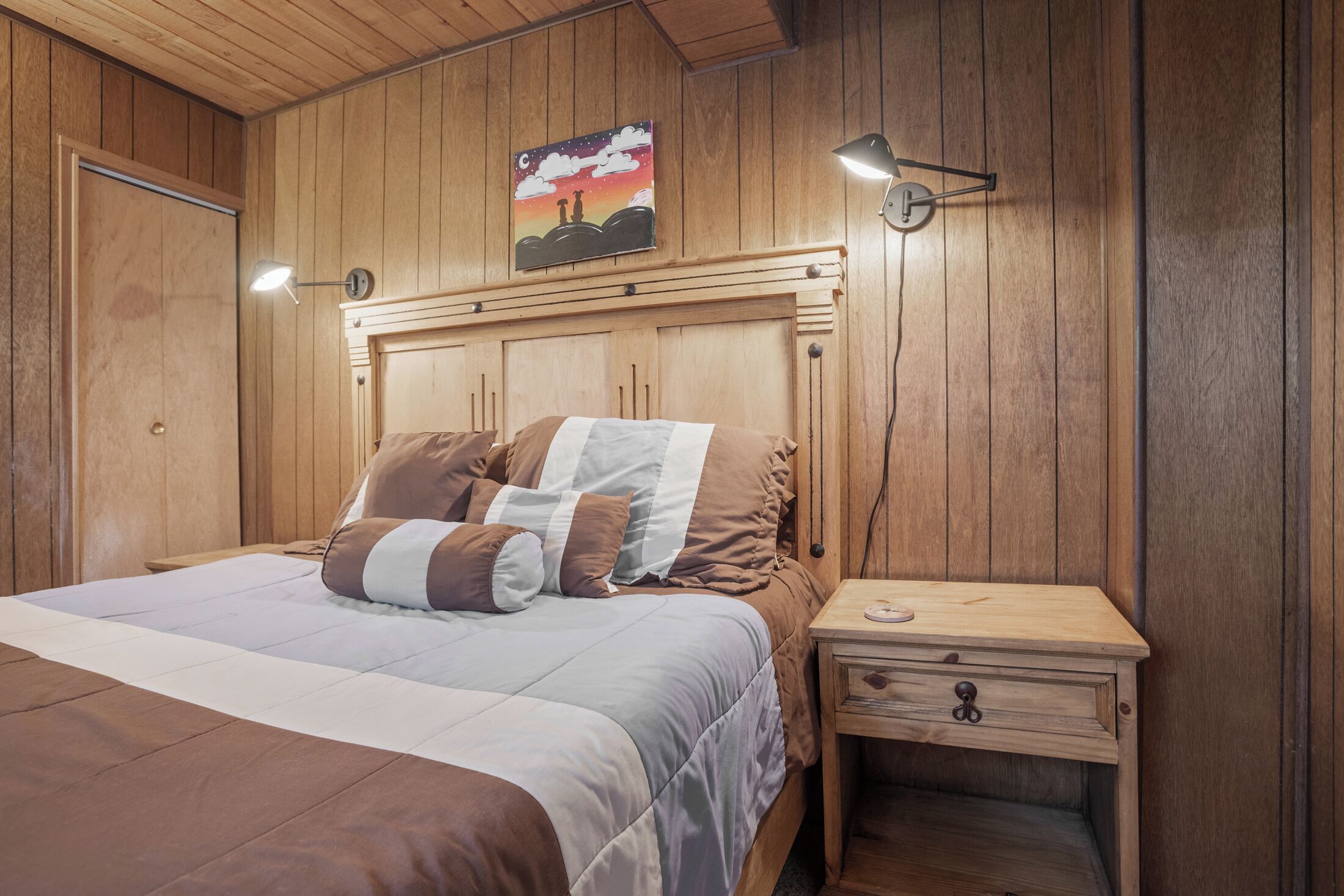 Un dormitorio con paneles de madera, una cama, una lámpara de noche y una mesita de noche con cajón.