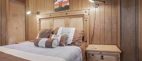 Un dormitorio con paneles de madera, una cama, una lámpara de noche y una mesita de noche con cajón.