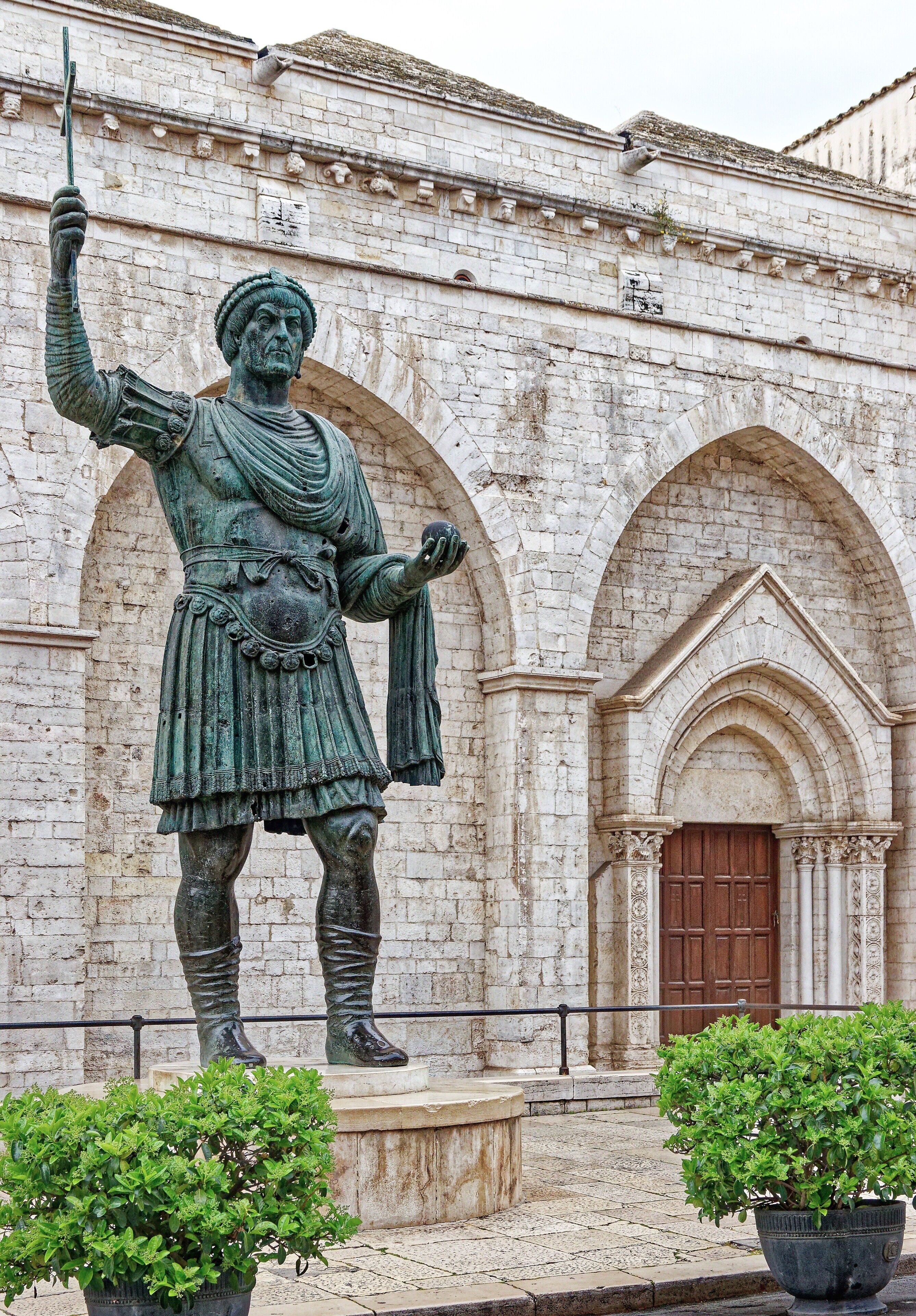 Eine Statue einer historischen Persönlichkeit in einem Innenhof mit einem dahinterliegenden Steinhaus.
