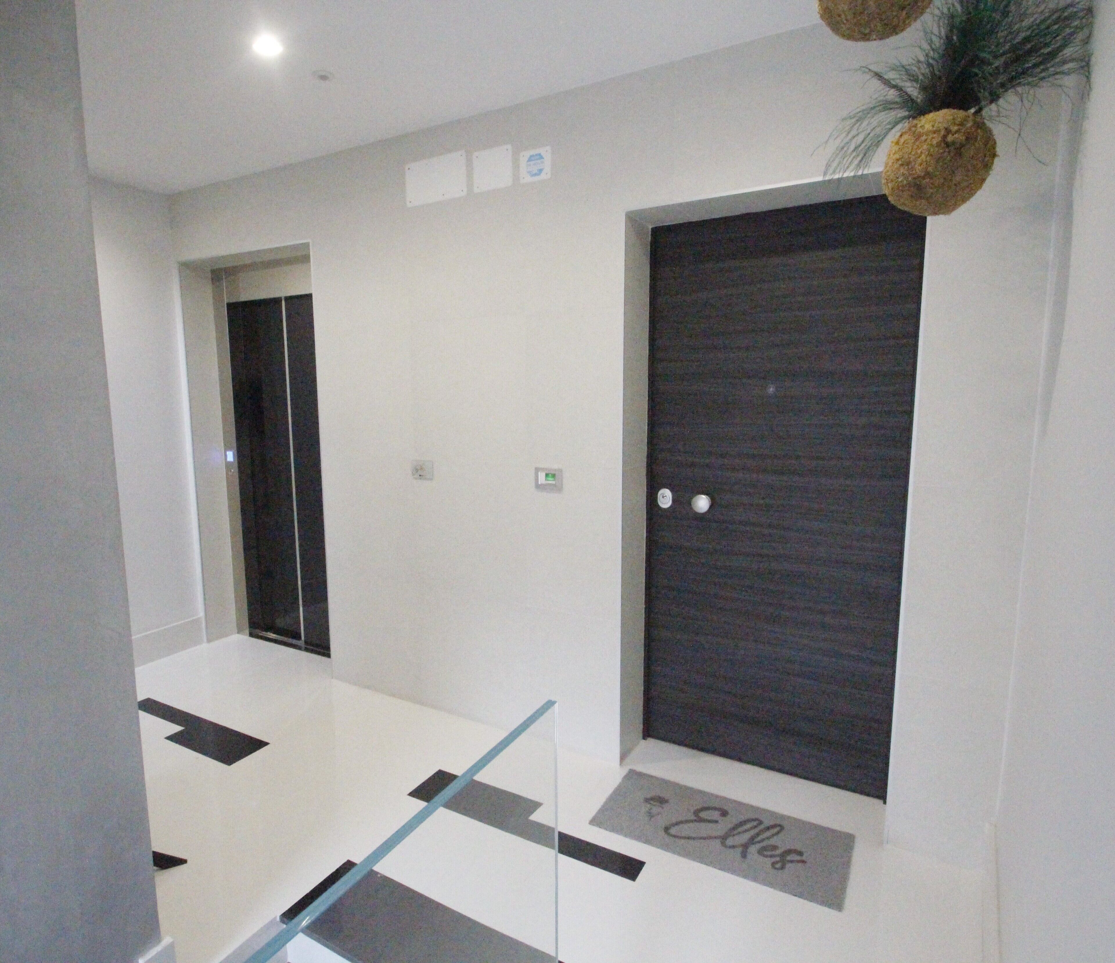 Um corredor moderno de hotel com uma porta de madeira escura, um painel de vidro e uma pequena placa no chão.