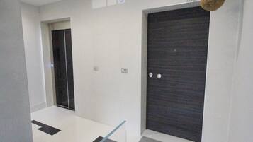 Um corredor moderno de hotel com uma porta de madeira escura, um painel de vidro e uma pequena placa no chão.