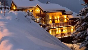 A large, multi-story wooden lodge with a snow-covered roof, surrounded by snow.