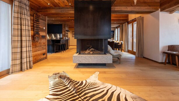 A spacious living area with a large fireplace, wooden ceiling, and a zebra rug on the floor.