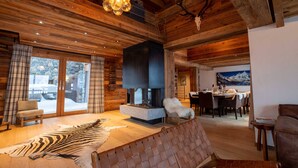 A cozy interior with a stone fireplace, wooden ceiling beams, a zebra rug, and a dining area with a mountain view.