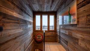 A wooden interior with a staircase leading to a balcony, a round bar counter, and a framed artwork on the wall.