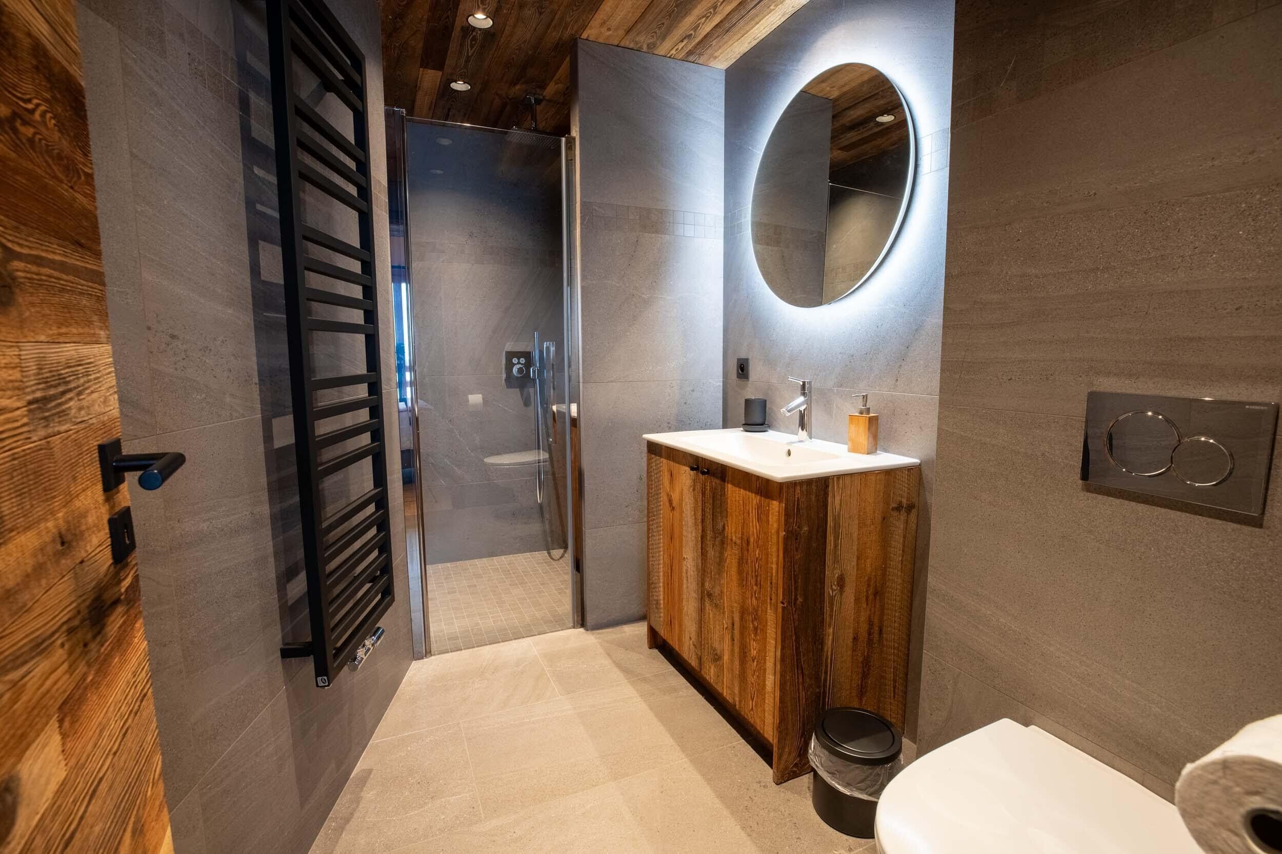 A modern bathroom with a wooden vanity, a round mirror, and a toilet.
