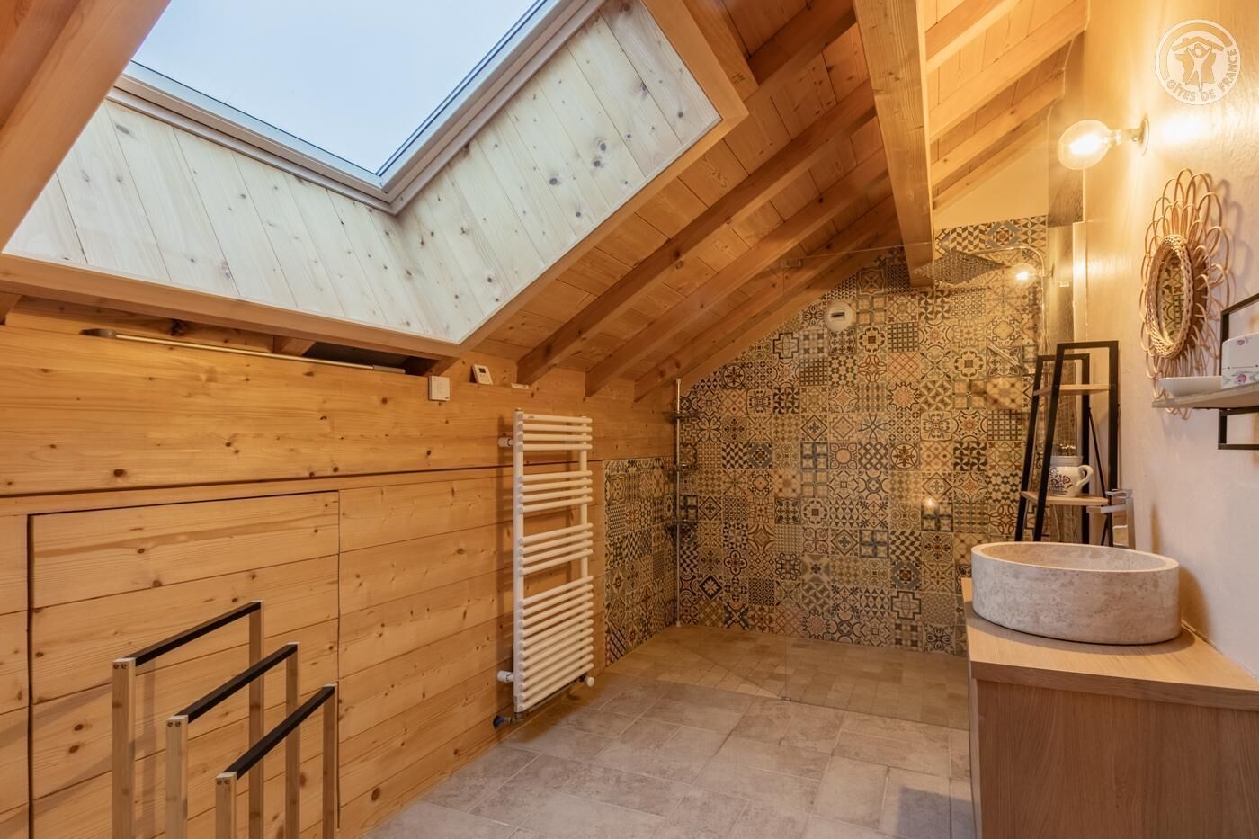 A wooden interior with a skylight, patterned tiles, a towel rack, and a sink.