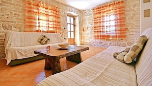 A cozy living room with a stone wall, a sofa, a coffee table, and striped curtains. - Lovely home in Tinjan with WiFi (Tinjan)