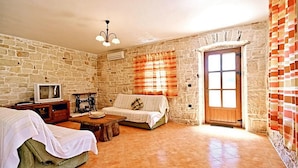 A rustic room with stone walls, a wooden door, a sofa, a small table, and a television. - Lovely home in Tinjan with WiFi (Tinjan)