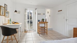 Een kamer met een wit bureau, een zwarte stoel, een houten bijzettafeltje en een bed.