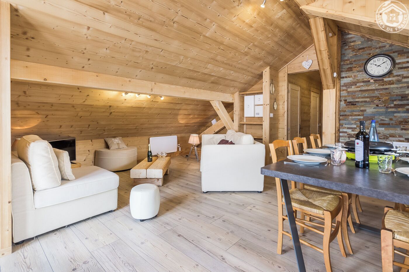 A cozy wooden interior with a dining area, sofas, and a clock on the wall.