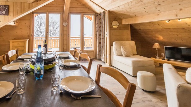 A wooden cabin interior with a dining table set for four, a sofa, and a TV. - LE Sapi - Albiez-montrond (ALBIEZ-MONTROND)