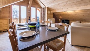 A wooden cabin interior with a dining table set for four, a sofa, and a television. - LE Sapi - Albiez-montrond (ALBIEZ-MONTROND)