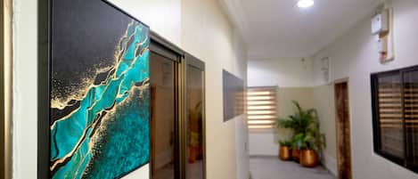 A hallway with a framed artwork, potted plants, and a ceiling light.