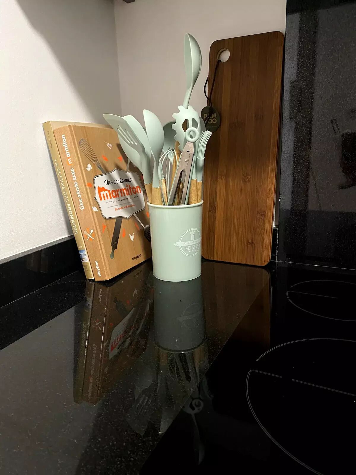 A kitchen counter with a box labeled 'Une autre aventure' and a cup holding various kitchen utensils.