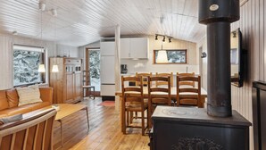 A cozy cabin interior with a wooden ceiling, a dining area with wooden chairs, a sofa with cushions, and a large window with a view of snow-covered trees. - Stunning home in Silkeborg with WiFi (Silkeborg)