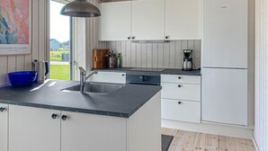 Une cuisine moderne avec des meubles blancs, un plan de travail noir, un évier en acier inoxydable, une machine à café et un réfrigérateur Siemens.