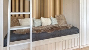 Une chambre de style « loft », avec un lit intégré, des lattes en bois et une échelle blanche.