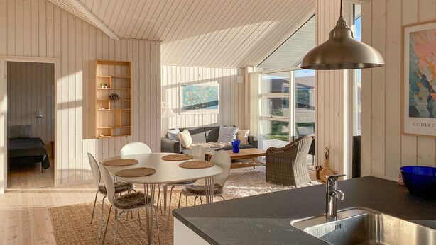 Une cuisine moderne dotée d’un grand îlot central, un coin repas avec des tables rondes et un espace de vie chaleureux avec un canapé et une bibliothèque.