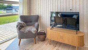 Un salon avec un fauteuil gris, un meuble TV en bois et un panier en osier.