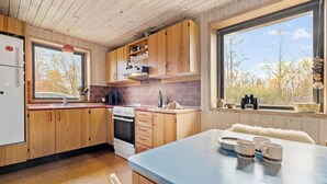 A modern kitchen with wooden cabinets, a built-in oven, and a large window offering a view of trees. - 3 bedroom beautiful home in ørsted (Ørsted)
