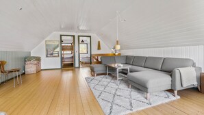 A spacious loft with a high ceiling, a grey sectional sofa, a wooden floor, and a white patterned rug. - 3 bedroom beautiful home in ørsted (Ørsted)