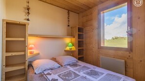 A cozy wooden cabin room with a bed, two bedside lamps, and a window with a view of a green landscape. - O'mikely - LE Dingo - Albiez Montrond (ALBIEZ MONTROND)